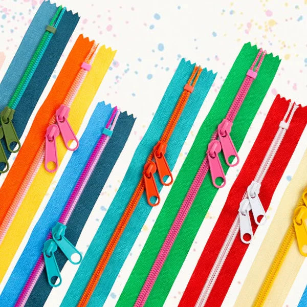 A promotional graphic showing multiple colorful zipper teeth profiles in different colors, including blue, green, yellow, orange, red, pink, and purple, arranged diagonally on a white background with the text 'NEW! ZIPPER COLORS' in orange and pink.
